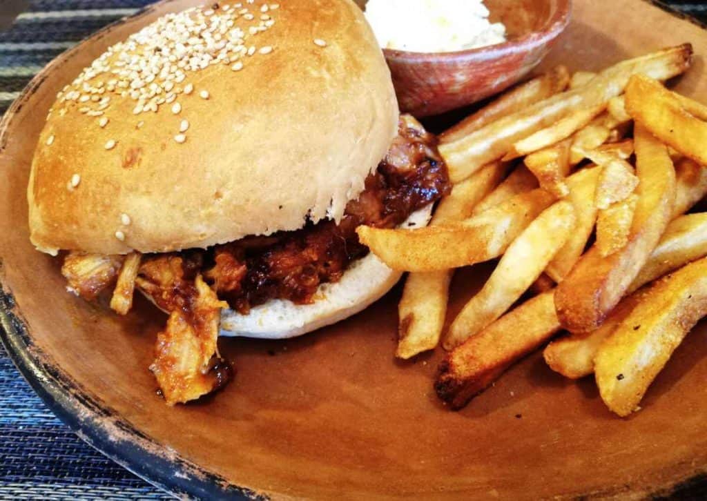 On a traditional clay play sits pork rib meat smothered in sauce between a hamburger bun with french fries at one of the best restaurants in San Cristobal de las Casas.