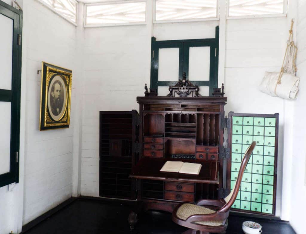 An interior view of the office at the Rafael Nunez House, complete with a desk, portrait, and rolled hammock hanging in the corner.