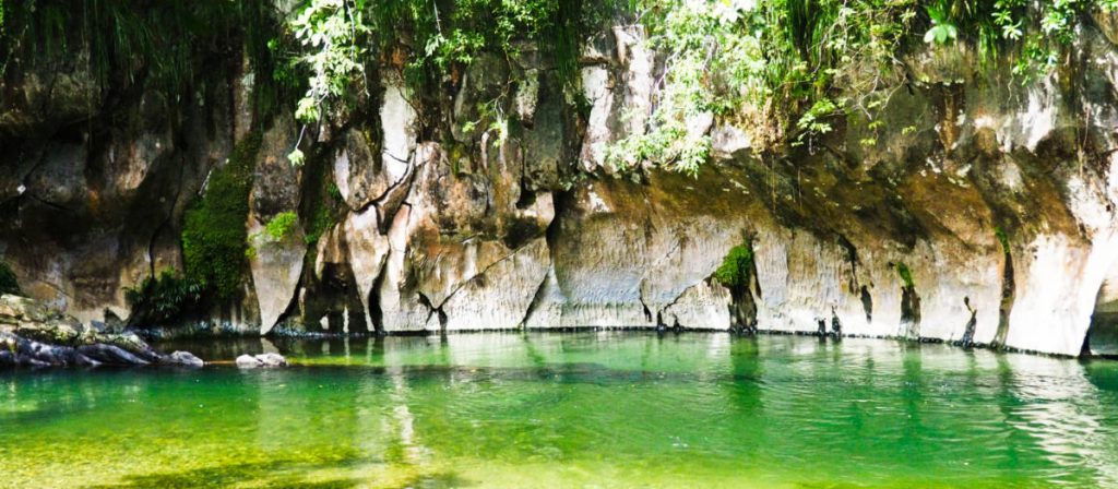 A curved bank of limestone rock lines the shallow water of Reserva Rio Claro Antioquia. The clear water appears green.