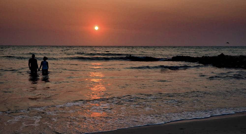 A couple walk into the ocean holding hands as the sun sets in Rincon del Mar