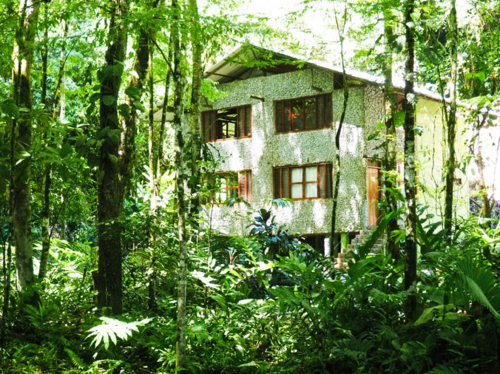A two story white stone building with wooden windows sits among the trees of Reserva Rio Claro, perfect for birdwatching.. 