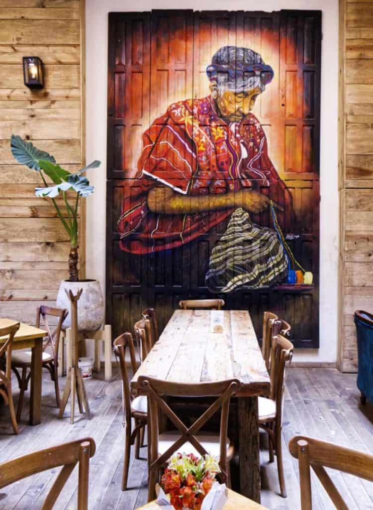 A dramatic floor to ceiling portrait of an indigenous woman weaving hangs from Sarajevo Cafe in San Cristobal. The room is also filled with several tables and a couch.