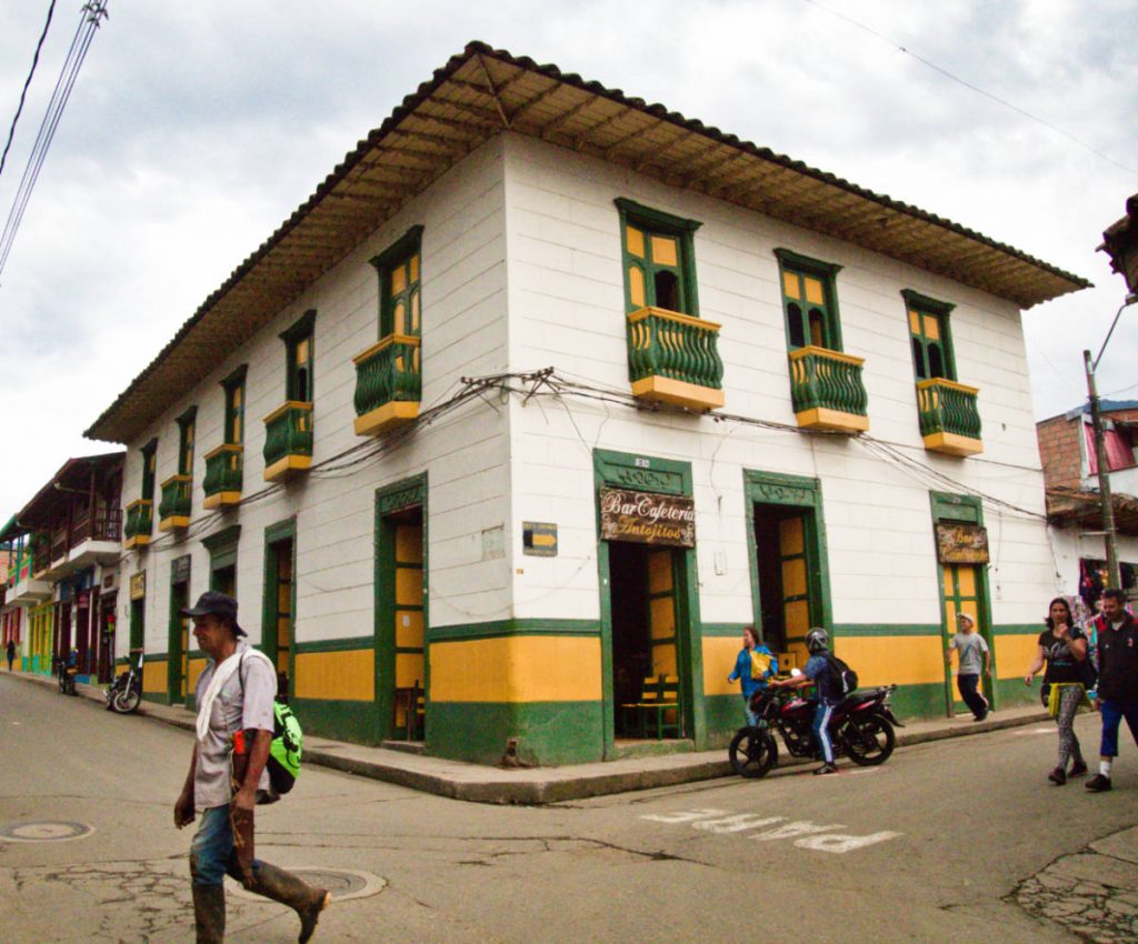 Street scene as people walk by a staple building in Jardin with green and yellow accents.