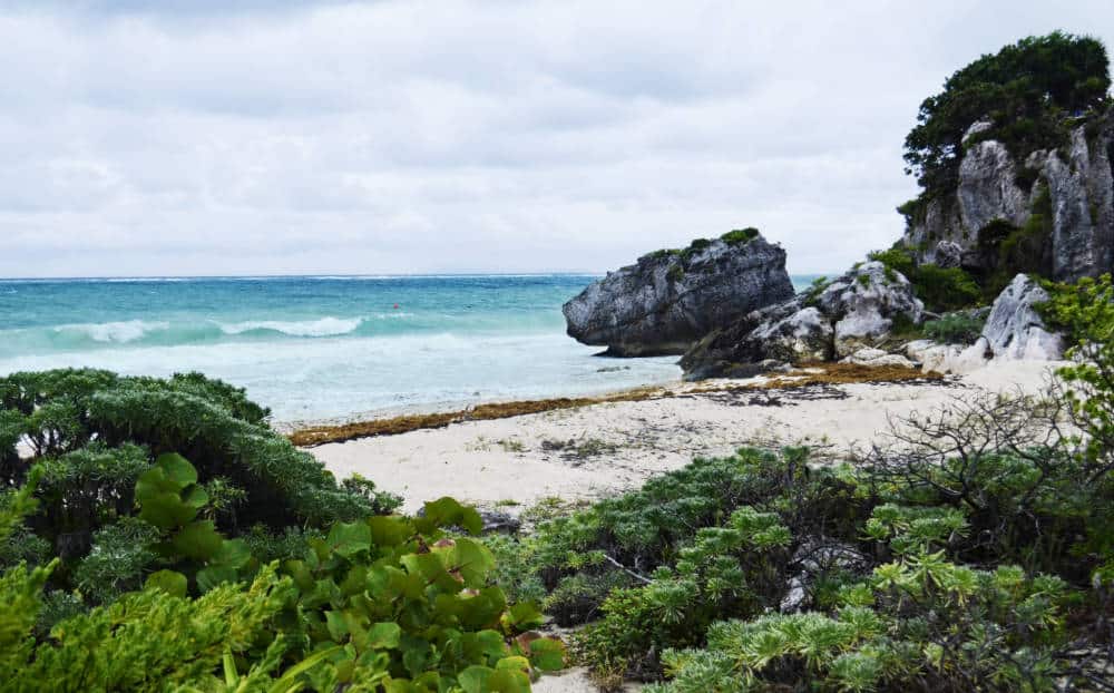 From the Tulum Mayan Ruins, a view of the cliff descending into the Caribbean Sea with sand in the foreground.