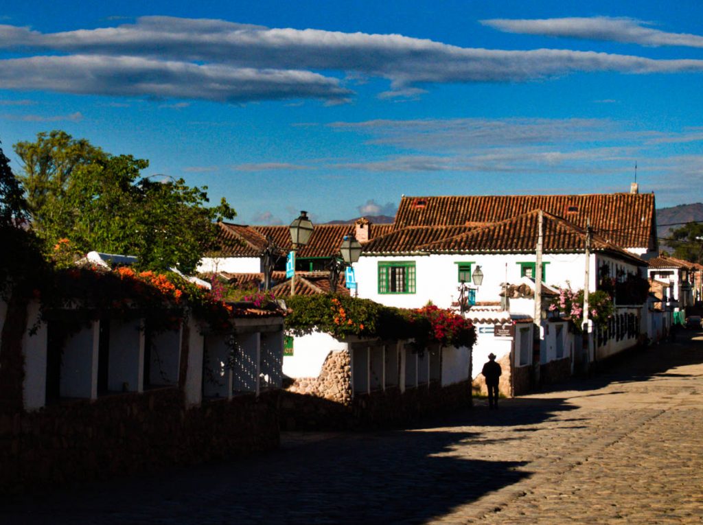 On the streets of Villa de Leyva, a man wearing a cowboy hat is silhouetted against the white colonial buildings as he walks through the streets.