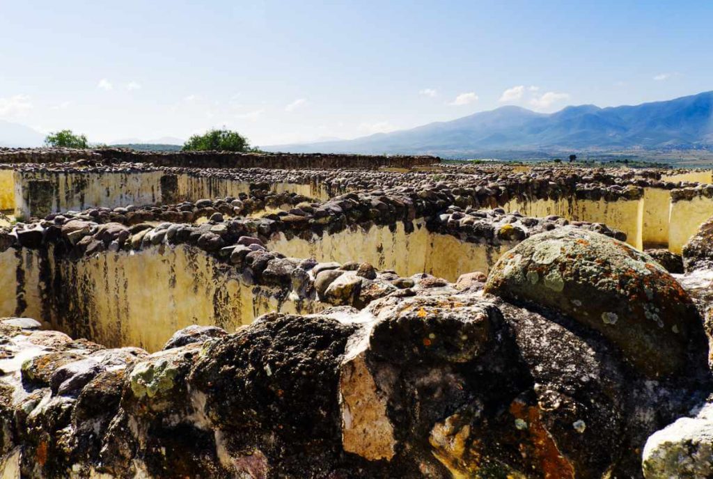 Cobbled stones emerge from the top of the labyrinth of walls at Yagul archaeological site, with mountain views in the background.